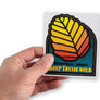 Male hand holding up bumper sticker with Tasmanian fagus (nothofagus gunnii)