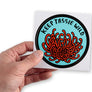 Male hand holding up large round bumper sticker featuring Tasmania's native waratah (telopea truncata)