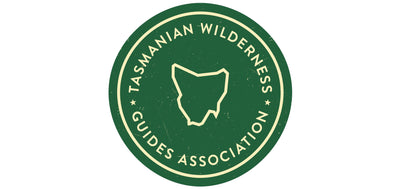 Tasmanian Wilderness Guides Association logo - a green circle with the name of the association and a  cream coloured outline of Tasmania in the middle.Green