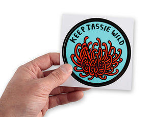 Male hand holding up large round bumper sticker featuring Tasmania's native waratah (telopea truncata)